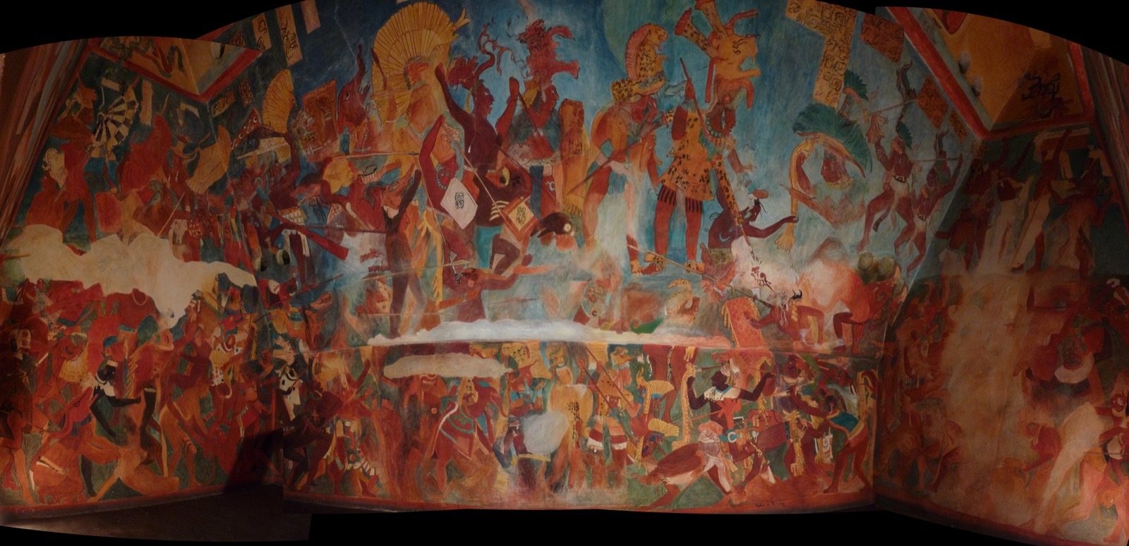A wide-angle reproduction of the Bonampak battle mural from Room 2, showing dozens of Maya warriors in elaborate feathered costumes in the chaos of combat, painted in reds, oranges, and blues, displayed at the Museo Nacional de Antropología in Mexico City.