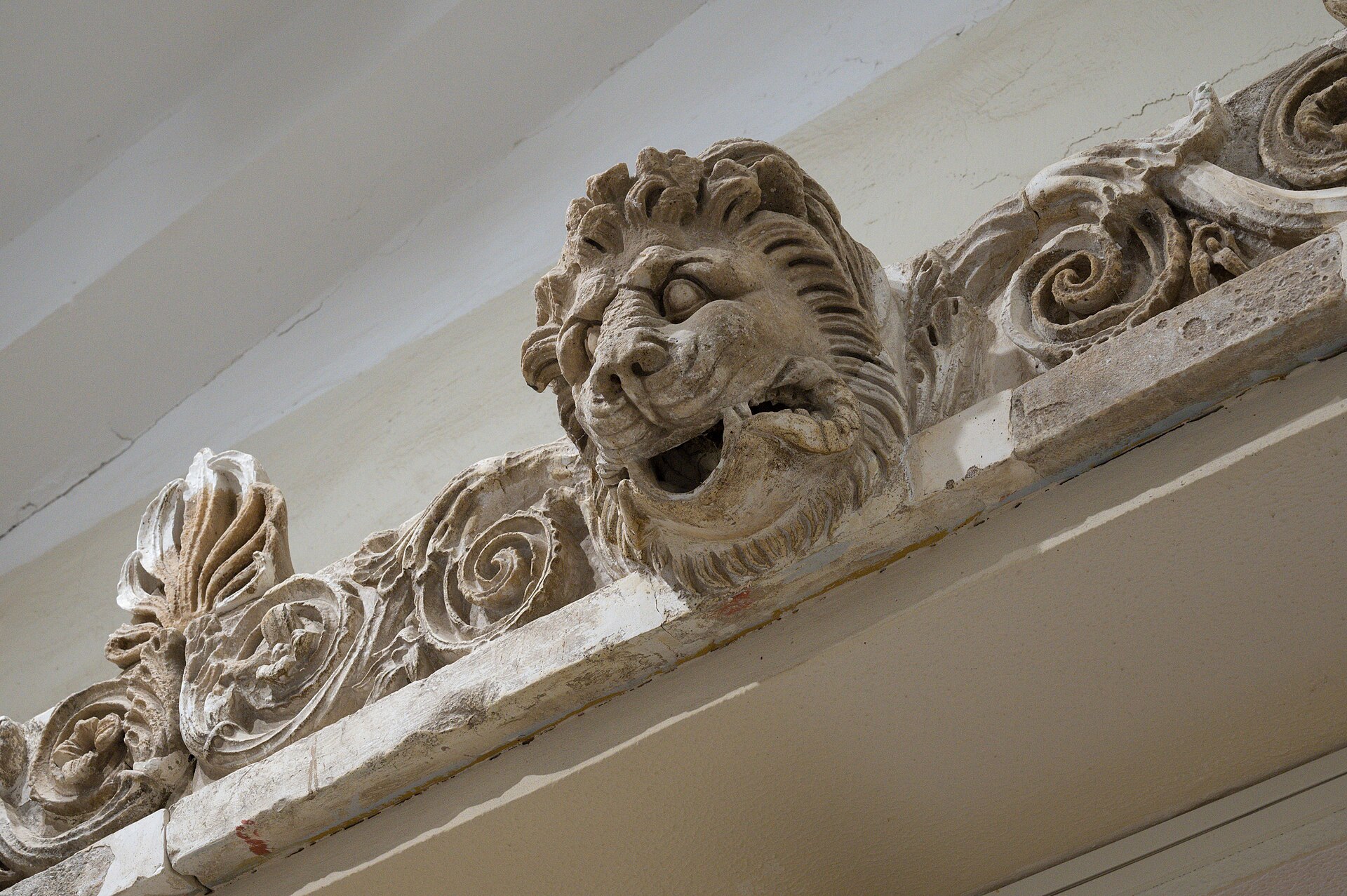 A carved lion-head waterspout on a scrolled cornice from the sanctuary of Asklepios at Epidauros, displayed in the Archaeological Museum of Epidaurus.